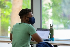 UF student with his computer and wearing a mask looking away.