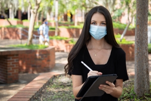 UF student looking at the camera wearing a mask holding a tablet