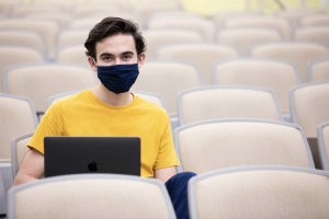 UF student looking at the camera while wearing a mask and holding a laptop