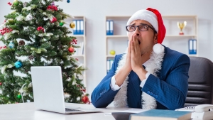 A man sits stressed at a desk while wearing a santa claus hat.