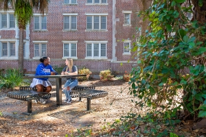 Two students talk at a table outdoors on the UF campus.