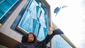UF student dressed in graduation regalia and throwing grad cap in the air